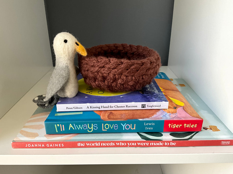 Stack of three children’s books from the ‘Love You No Matter What’ WonderBundle™, topped with a felt seagull plush, Sol, and a handwoven brown nest. Titles include I’ll Always Love You, A Kissing Hand for Chester Raccoon, and The World Needs Who You Were Made to Be.