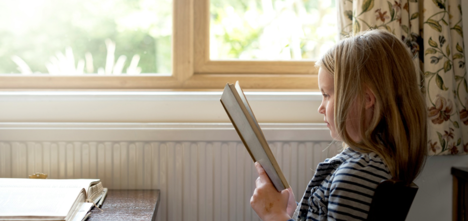 A young girl reading a book by a sunlit window — story-centered formation through Wonder & Wisdom Books.
